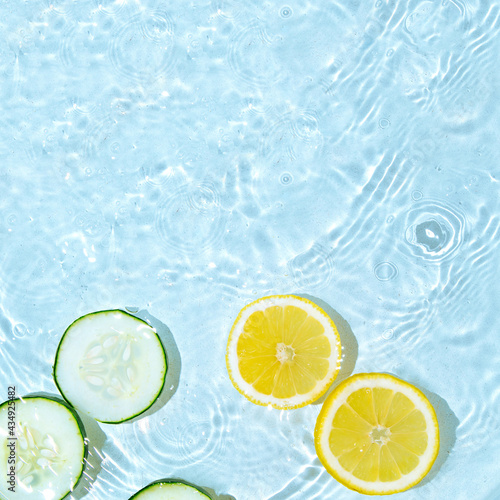 Minimal concept of lemon and cucumber in water. Place for text. Copy space. Summer scene. Squeezing the juice.