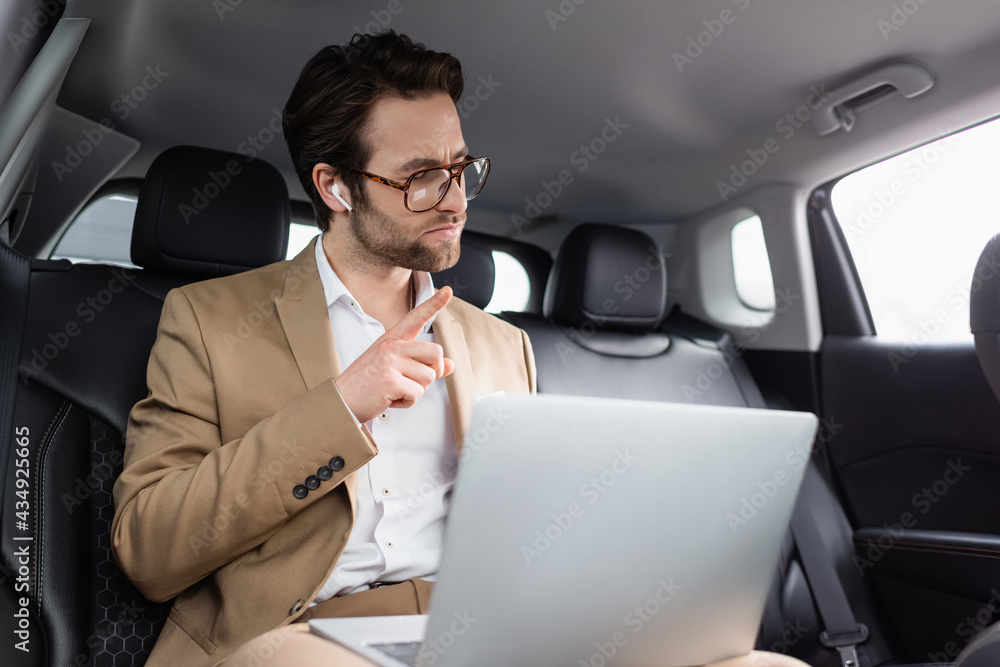 businessman in glasses and wireless earphones pointing with finger during video call in car