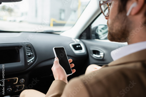 blurred man in glasses holding smartphone with blank screen in car