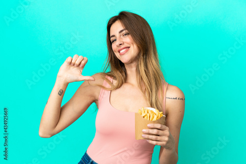 Caucasian woman holding fried chips isolated on blue background proud and self-satisfied
