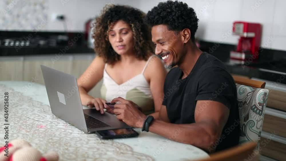 African descent couple browsing laptop together at home kitchen African descent couple browsing laptop together at home kitchen