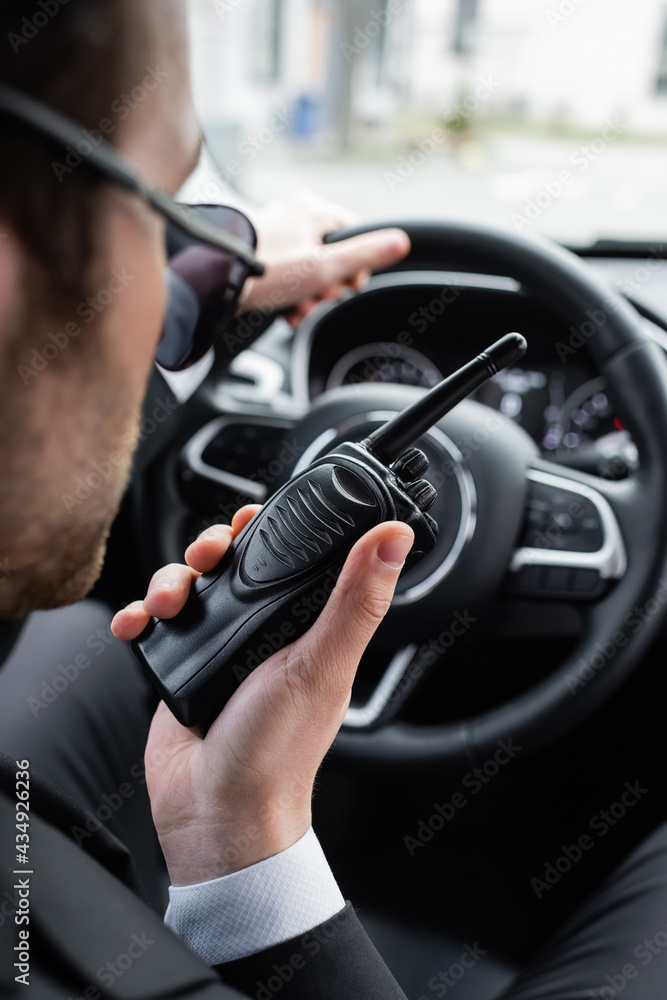 blurred bodyguard in sunglasses using walkie talkie in car