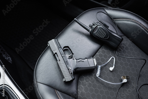 top view of walkie talkie, black gun and security earpiece on car seat