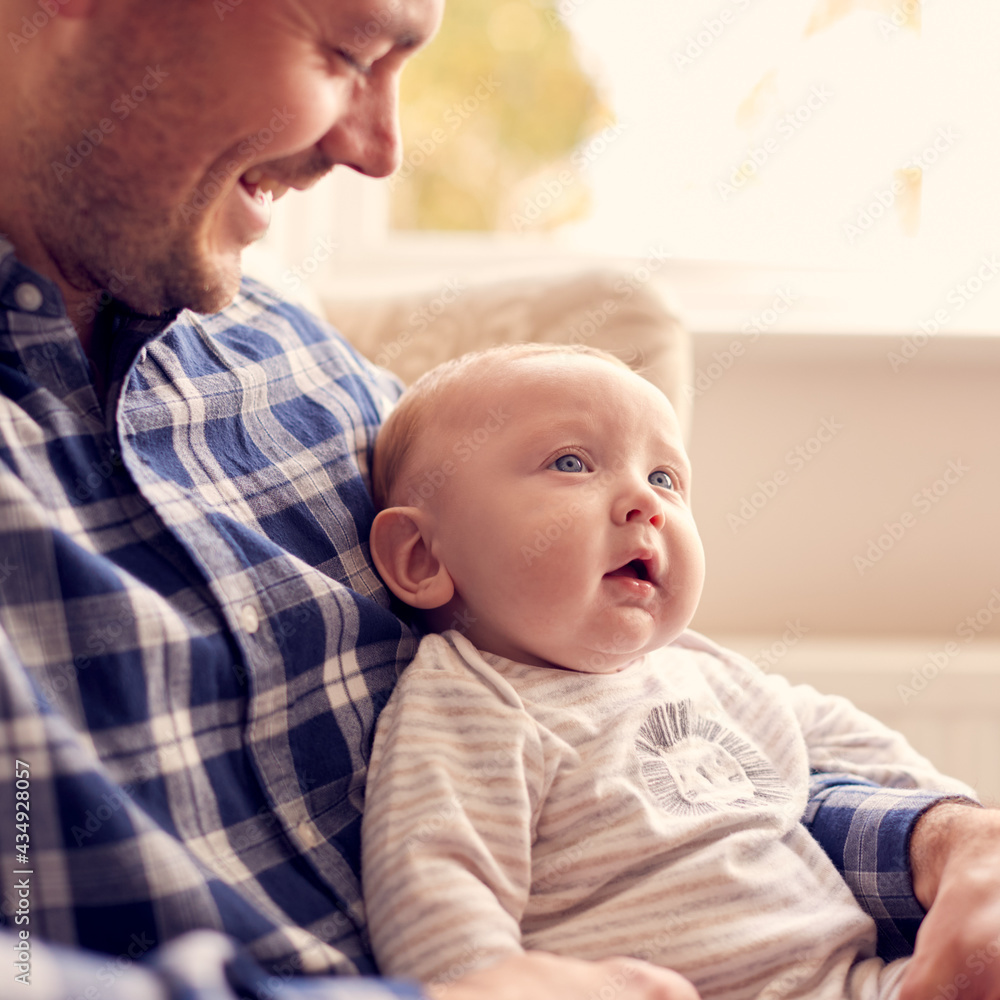 Close Up Of Father Cuddling Baby Son Sitting On Lap In Lounge Chair At Home Together Close Up Of Father Cuddling Baby Son Sitting On Lap In Lounge Chair At Home Together