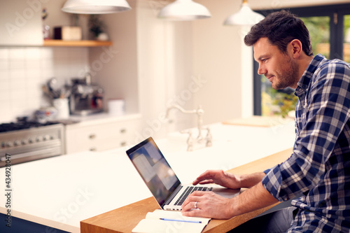 Man Working From Home Using Laptop On Kitchen Counter