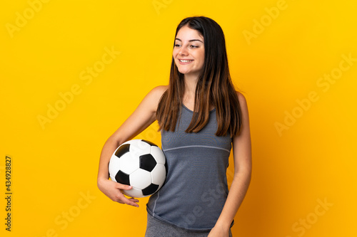 Young football player woman isolated on yellow background looking to the side and smiling © luismolinero