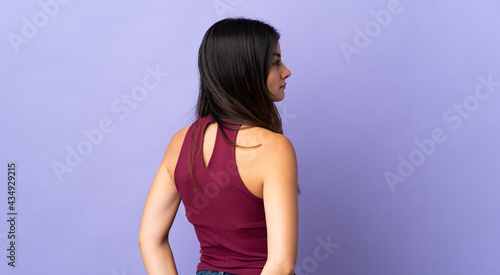 Young caucasian woman isolated on purple background in back position and looking back