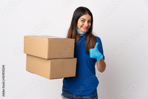 Young delivery woman protecting from the coronavirus with a mask isolated on white background with thumbs up because something good has happened