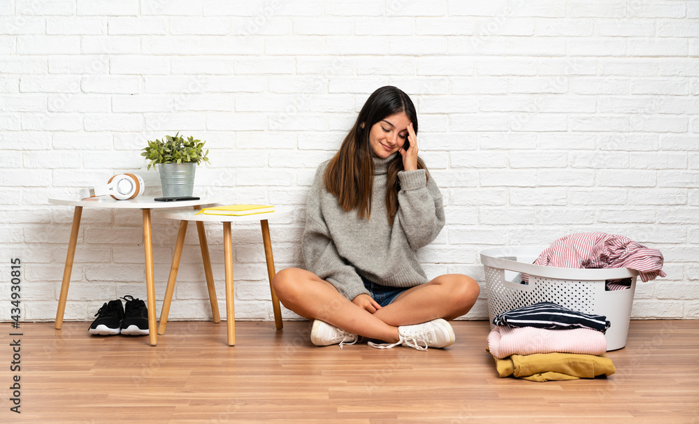 Young woman sitting on the floor at indoors with clothes basket laughing Young woman sitting on the floor at indoors with clothes basket laughing