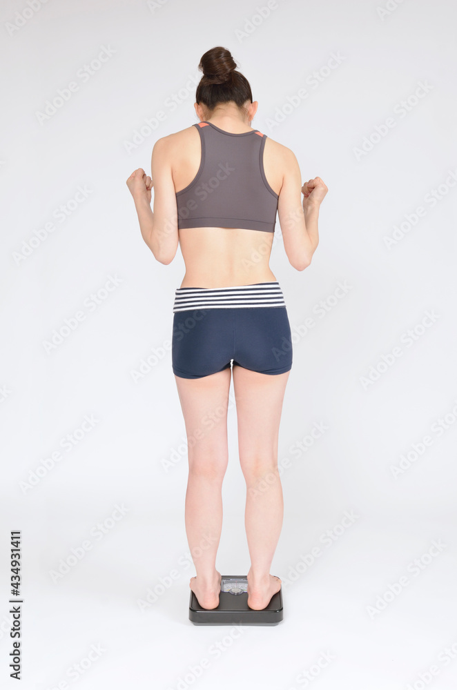 体重計に乗ってガッツポーズする若い女性 体重計に乗ってガッツポーズする若い女性