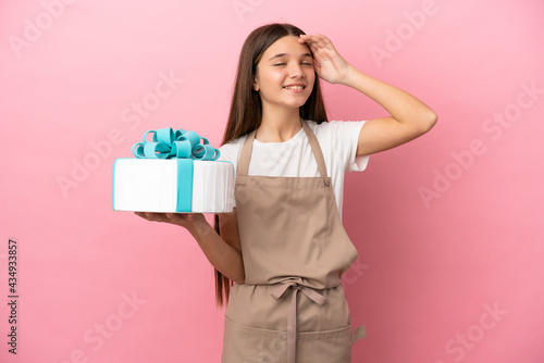 Little girl with a big cake over isolated pink background smiling a lot