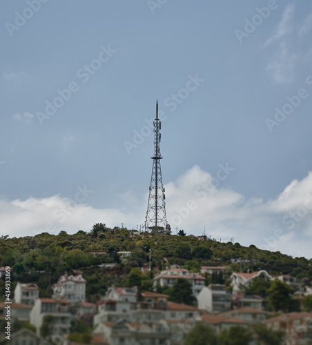 Telecommunication tower over town buildings and houses. High frequency receiver on the island with summer sky. Telephone and television antenna near living apartments.