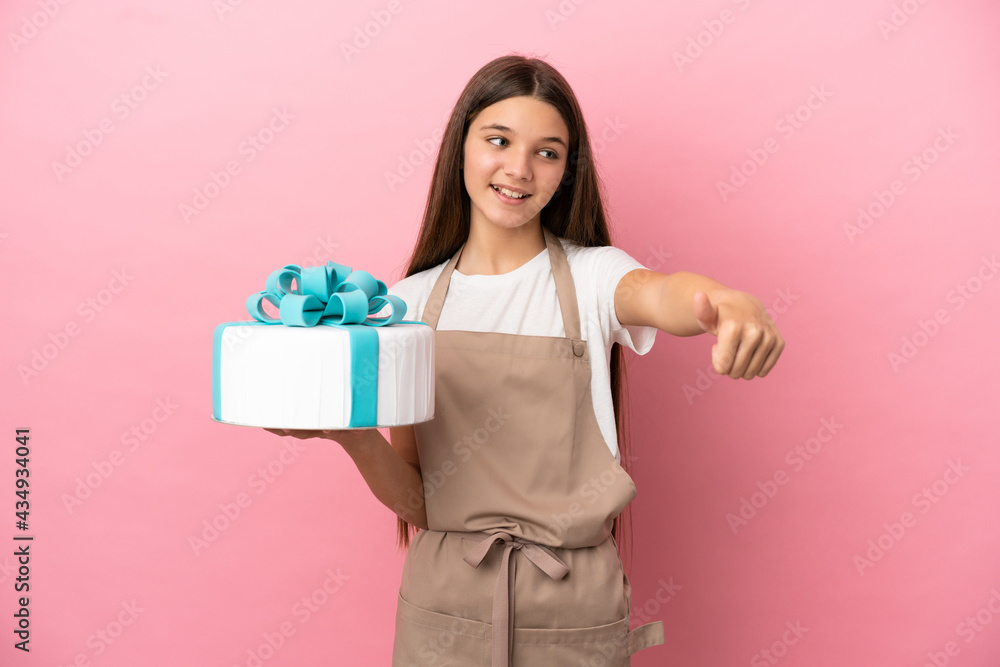 Little girl with a big cake over isolated pink background giving a thumbs up gesture Little girl with a big cake over isolated pink background giving a thumbs up gesture
