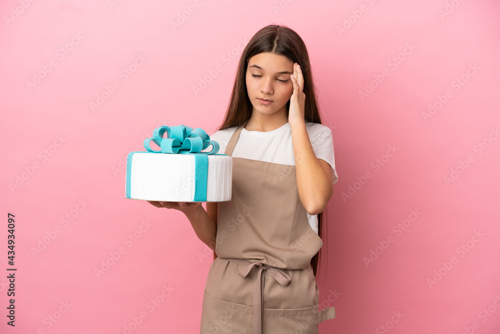 Little girl with a big cake over isolated pink background with headache Little girl with a big cake over isolated pink background with headache