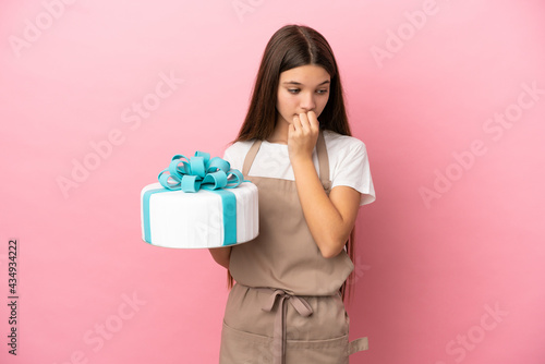 Little girl with a big cake over isolated pink background having doubts