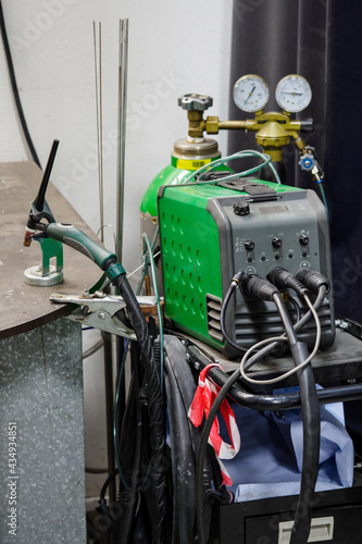 Tig welder with a torch in a stand and bottles in the background.
