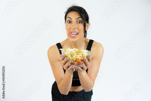 Profile portrait positive healthy woman in white sportswear holding big bowl with fresh vegetable salad. Healthy nutrition.
