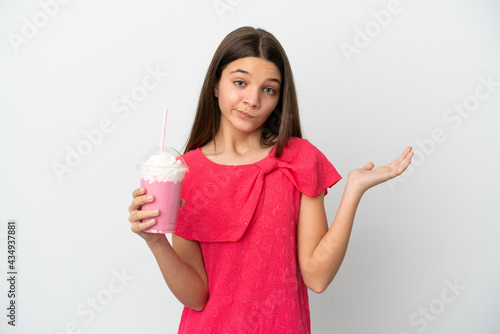 Little girl with strawberry milkshake over isolated white background having doubts while raising hands