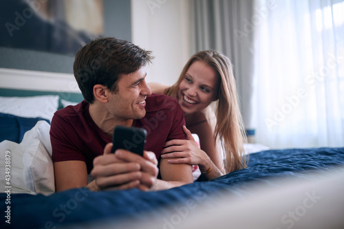 young caucasian couple laying in bed , smiling, laughing, enjoying, having a good time.