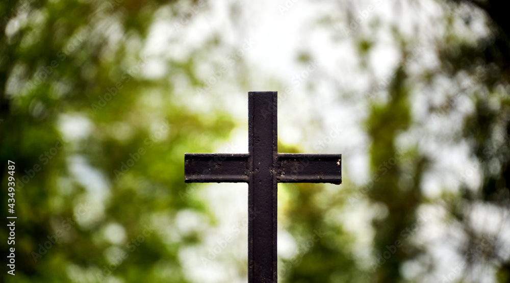 Black cast iron Christian cross isolated against intentionally blurred background