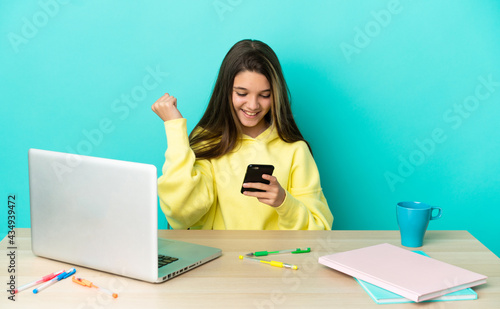 Little girl in a table with a laptop over isolated blue background surprised and sending a message