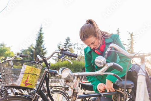 Murais de parede Young woman outdoor locking oe unlocking bicycle using green sustainable transpo