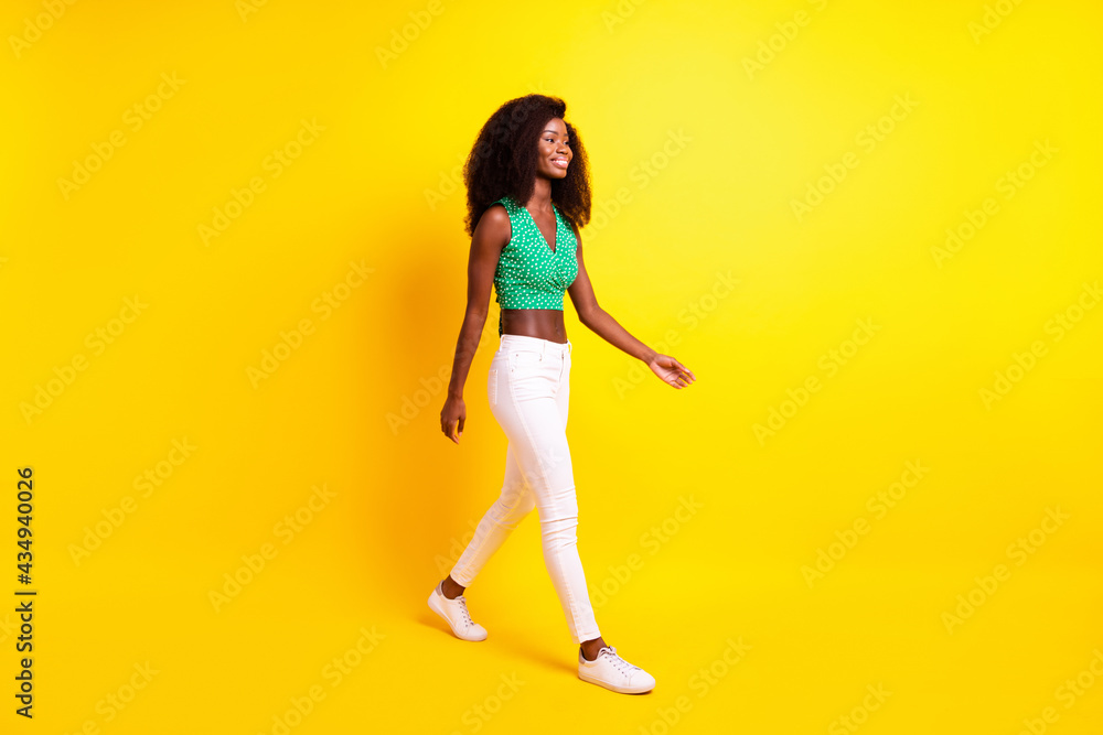 Full length body size photo funky girl smiling walking forward in stylish clothes isolated vivid yellow color background