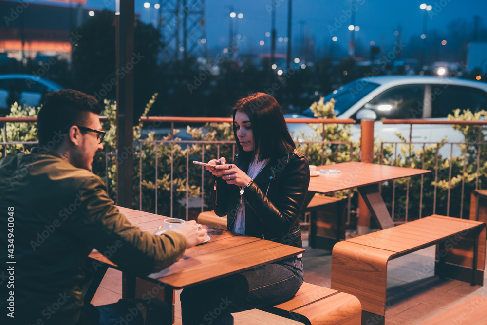 Young couple at night sitting cafe taking photo of coffee cup sharing on social media