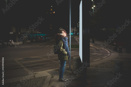 Young woman at night reading news on glowing information billboard outdoor