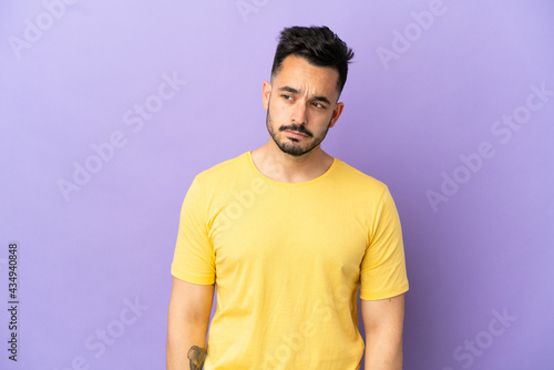 Young caucasian man isolated on purple background having doubts while looking side