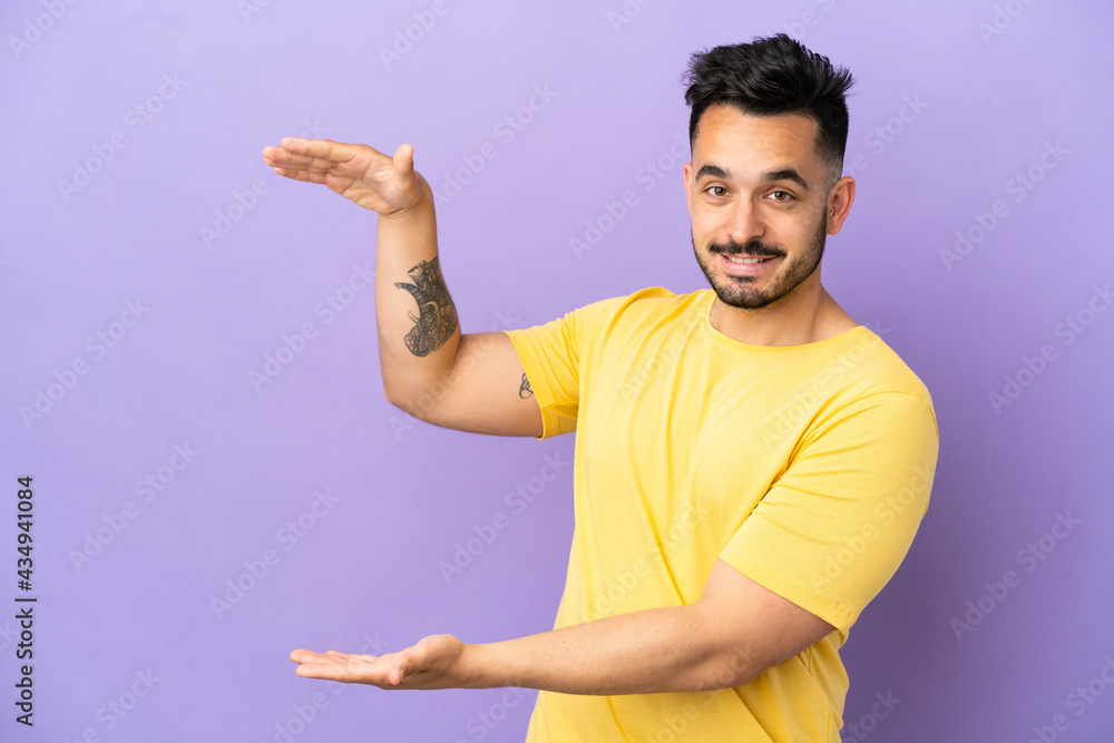 Young caucasian man isolated on purple background holding copyspace to insert an ad