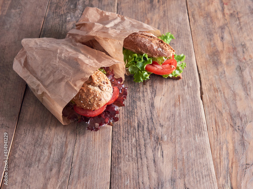 two vegetable baguettes on paper bags, isolated on a wooden table