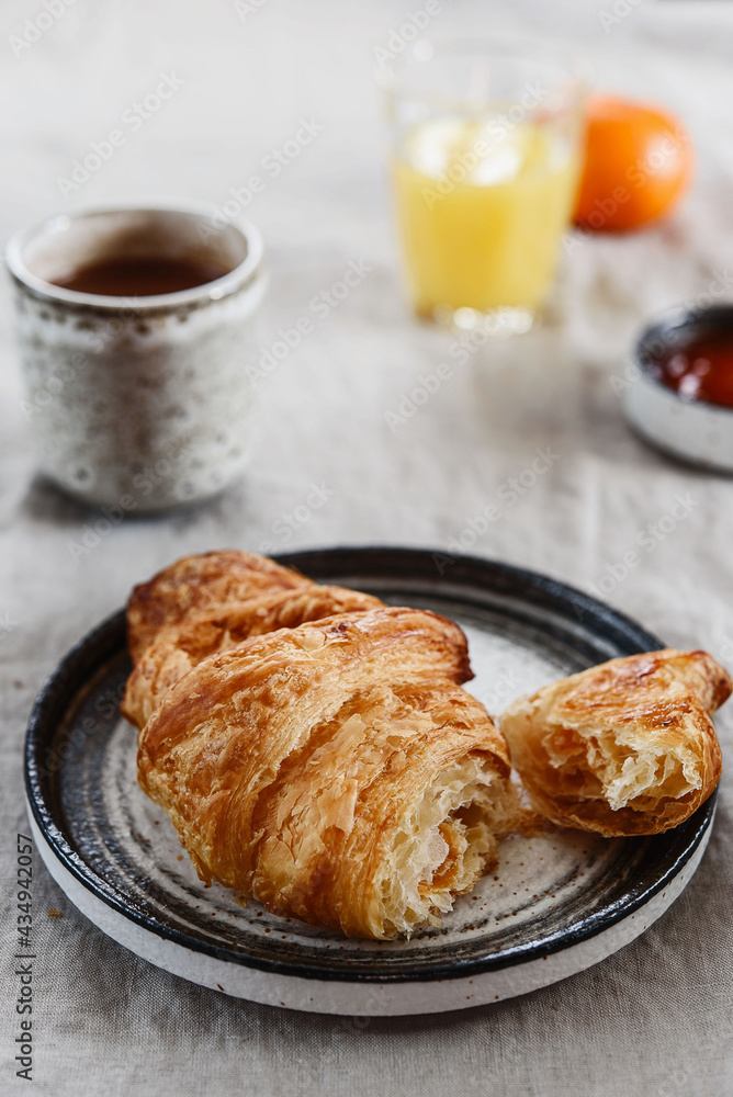 Breakfast with croissant, jam and hot chocolate, juice and tangerine on greige linen tablecloth. Selective focus Breakfast with croissant, jam and hot chocolate, juice and tangerine on greige linen tablecloth. Selective focus