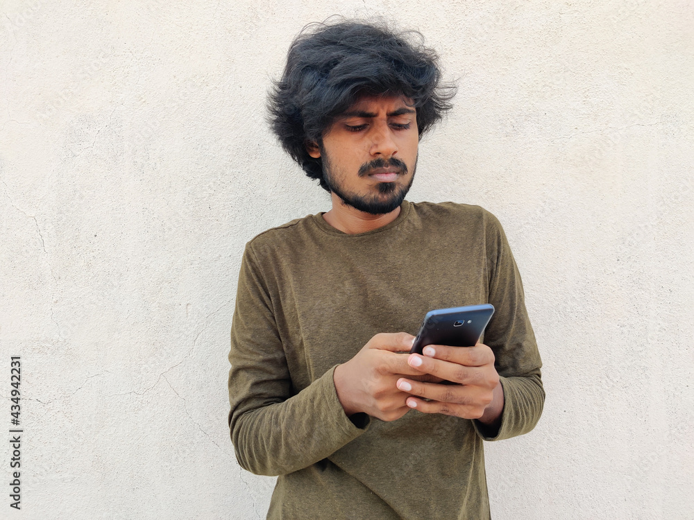 Fototapeta premium Serious looking south indian beard man using his smart phone. He is ordering something. White background