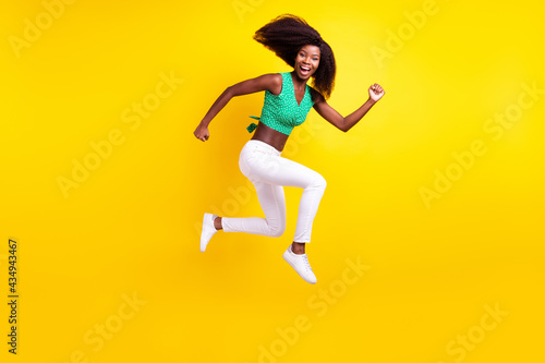 Full length body size photo young girl jumping running laughing overjoyed isolated vibrant yellow color background