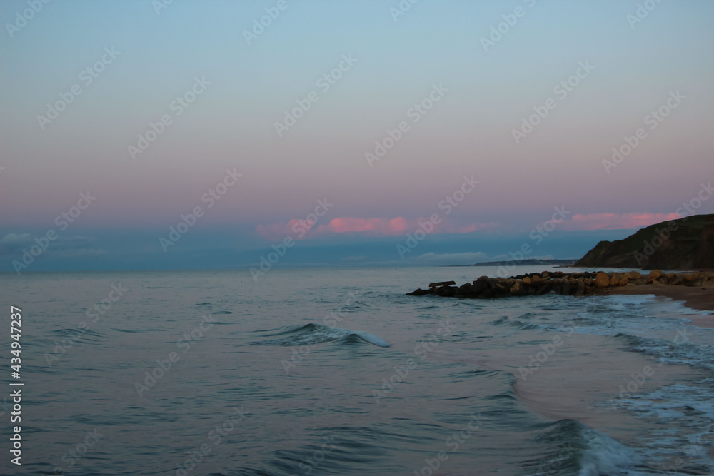 Azure sea with pink clouds from the sunset reflex on the horizon