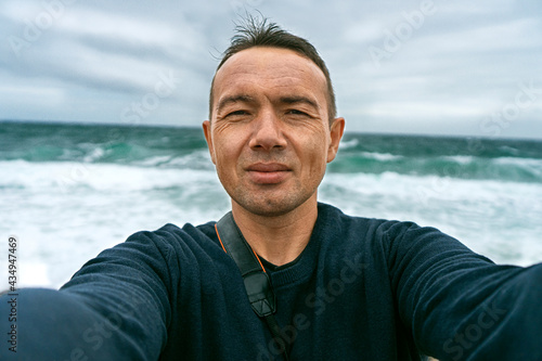 A man takes pictures of himself with a camera against the background of the turquoise sea