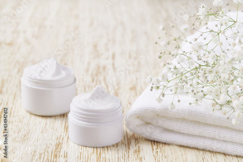 Natural face cream or lotion  organic cosmetic to moisturize the skin with towel and flowers in the background.