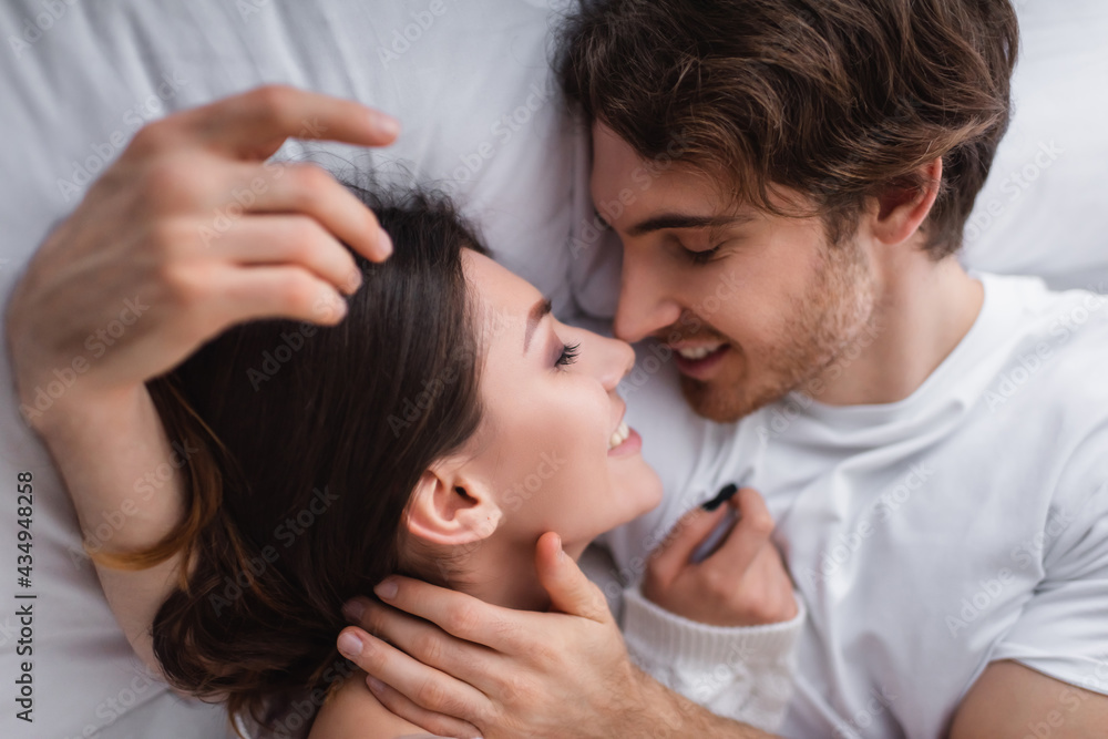 Top view of smiling couple hugging on white bedding Top view of smiling couple hugging on white bedding