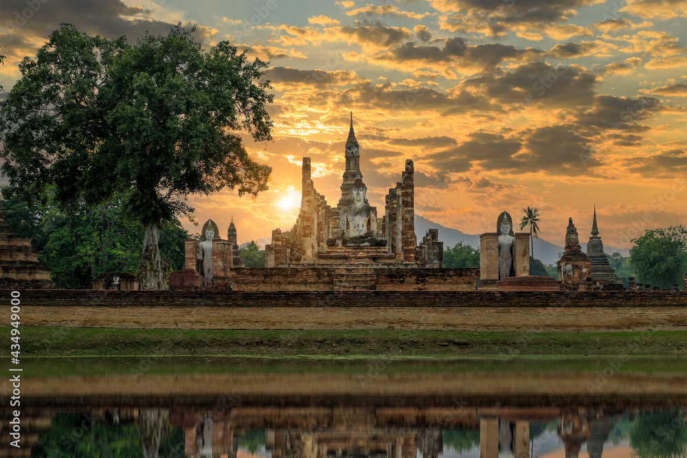 Buddha statue and pagoda Wat Mahathat temple with reflection during dramatic sky sunset, Sukhothai Historical Park, Thailand