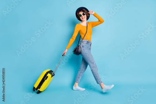 Full size profile photo of optimistic brunette short hairdo lady go with bag wear shirt jeans sneakers isolated on blue color background