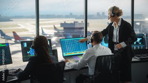 Female and Male Air Traffic Controllers with Headsets Talk in Airport Tower. Office Room is Full of Desktop Computer Displays with Navigation Screens, Airplane Departure and Arrival Data for the Team. photo