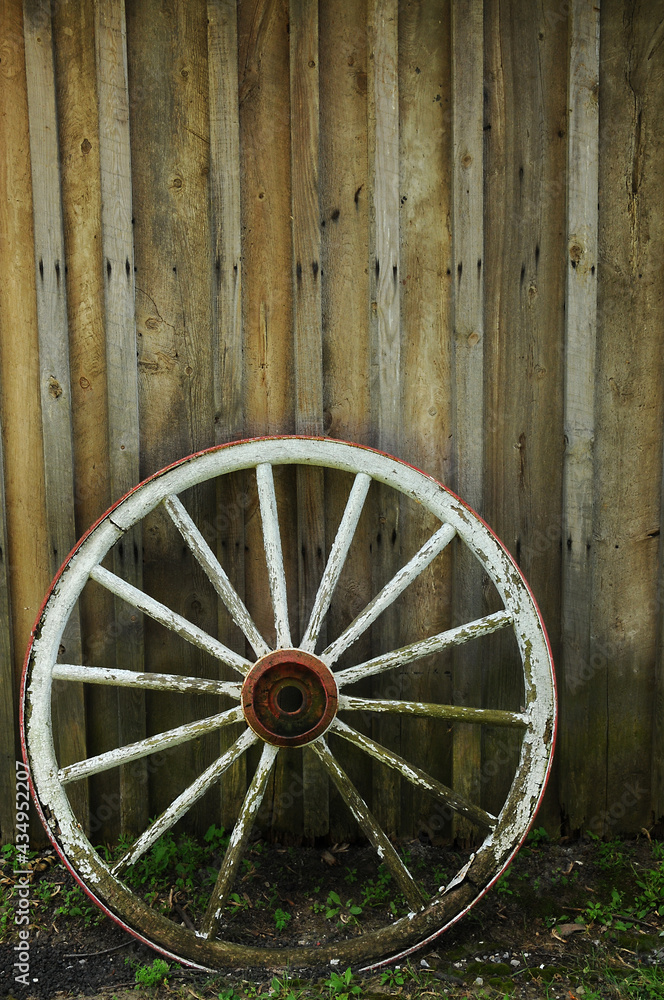 old white wooden carriage wheel and spokes besides a wooden building
