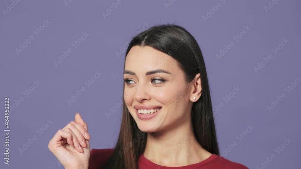 A charming young woman is posing to the camera standing isolated over a purple background in the studio A charming young woman is posing to the camera standing isolated over a purple background in the studio