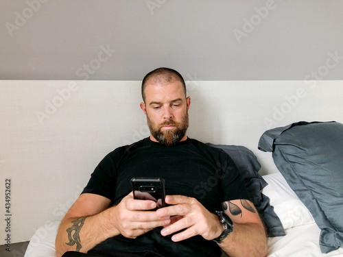Bearded man laying in bed using his mobile phone © sashapritchard
