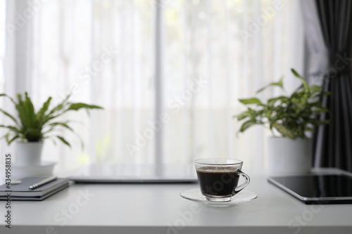 Black tea in glass cup on and black tablet with plants pot on white desk