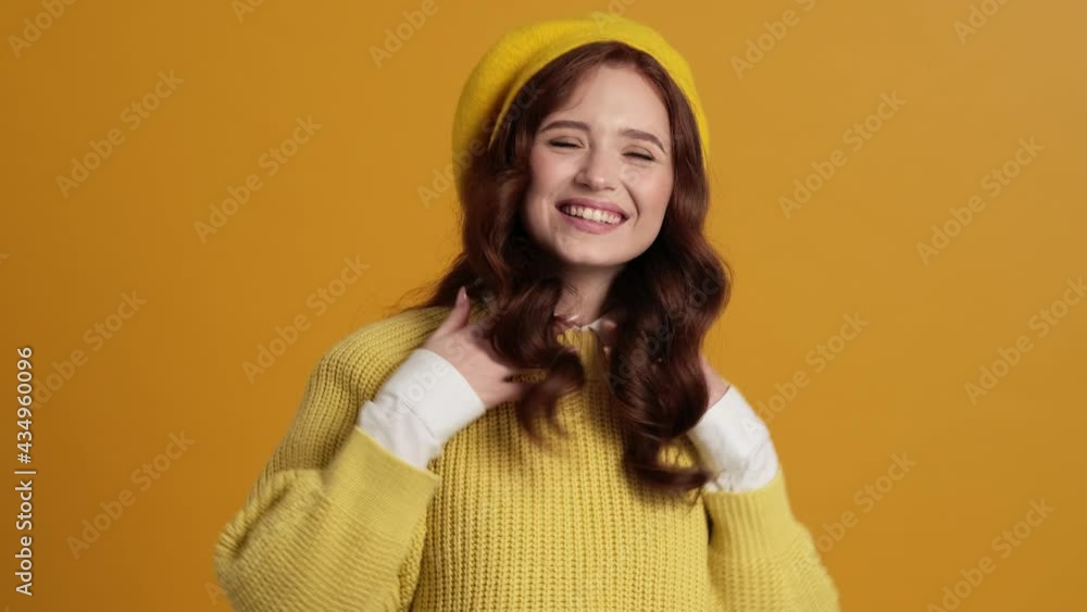 A smiling woman in a beret showing thumb-up gesture while standing in the yellow studio A smiling woman in a beret showing thumb-up gesture while standing in the yellow studio