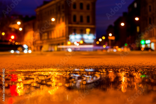 Nights lights of the big city  the night intersection between the houses on which cars travel. Close up view  of a puddle on the level of the hatch