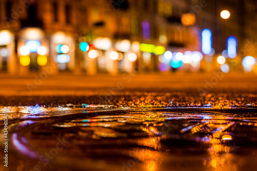 Nights lights of the big city, the night street. Close up view of a puddle on the level of the hatch