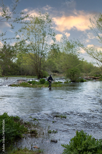 young man with high rubber boots for water wading the river with a fishing rod in search of fish and trouts